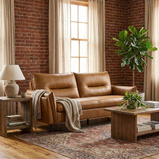 Brown leather sofa in a living room with brick walls, wooden coffee table, and decorative items.