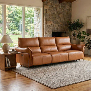 Brown leather sofa in a living room with stone fireplace and large windows.