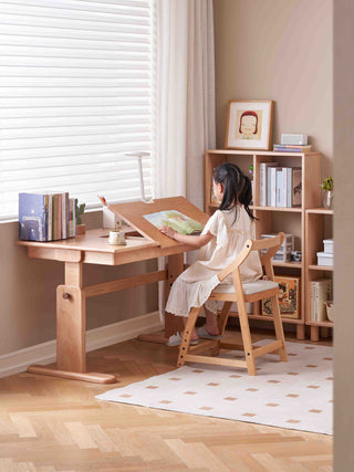 Child sitting at a wooden desk in a home office setting with a bookshelf and window blinds.