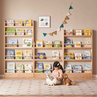 Child sitting on the floor reading a book in front of a wooden bookshelf filled with books.