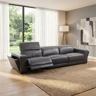 Grey leather sofa in a living room with large windows and a rug.