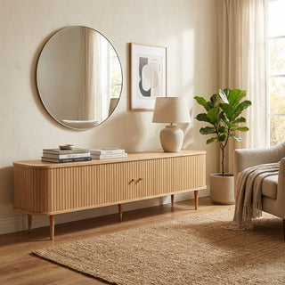 Living room with wooden tv console, round mirror, lamp, and plant.