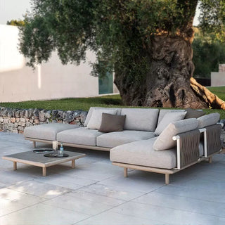 Outdoor patio with a modern gray sectional sofa and coffee table, surrounded by greenery.