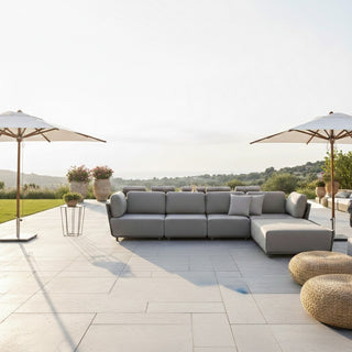 Outdoor patio with gray sectional sofa, umbrellas, and plants on a sunny day.