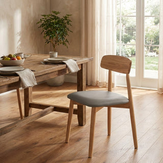 Wooden dining table with chairs in a bright room with large windows.
