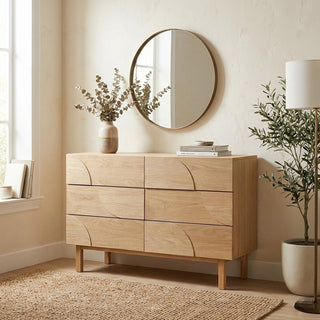 Wooden dresser in a room with a round mirror, plants, and a lamp.