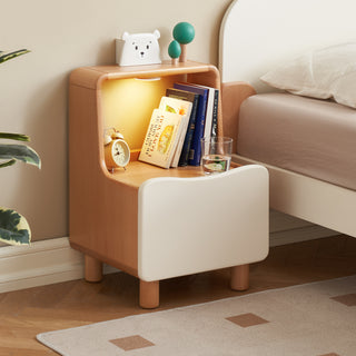Wooden nightstand with books, glass, and decor items next to a bed.